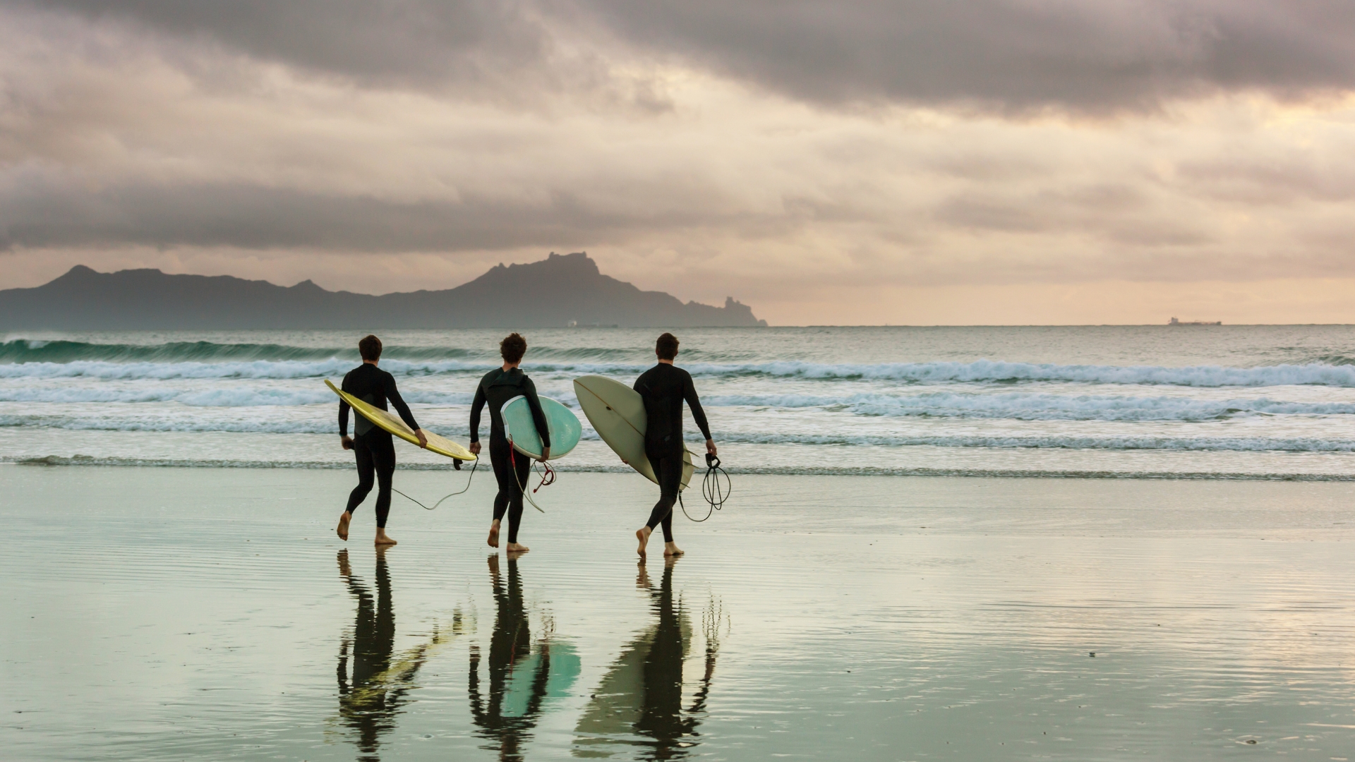Three surfers carrying their boards into the sea at dawn.